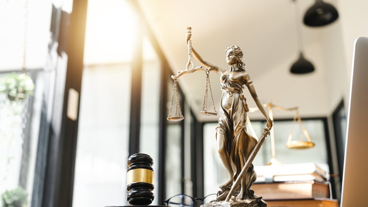 Schreibtisch mit Richterhammer und einer Justitia-Statue.