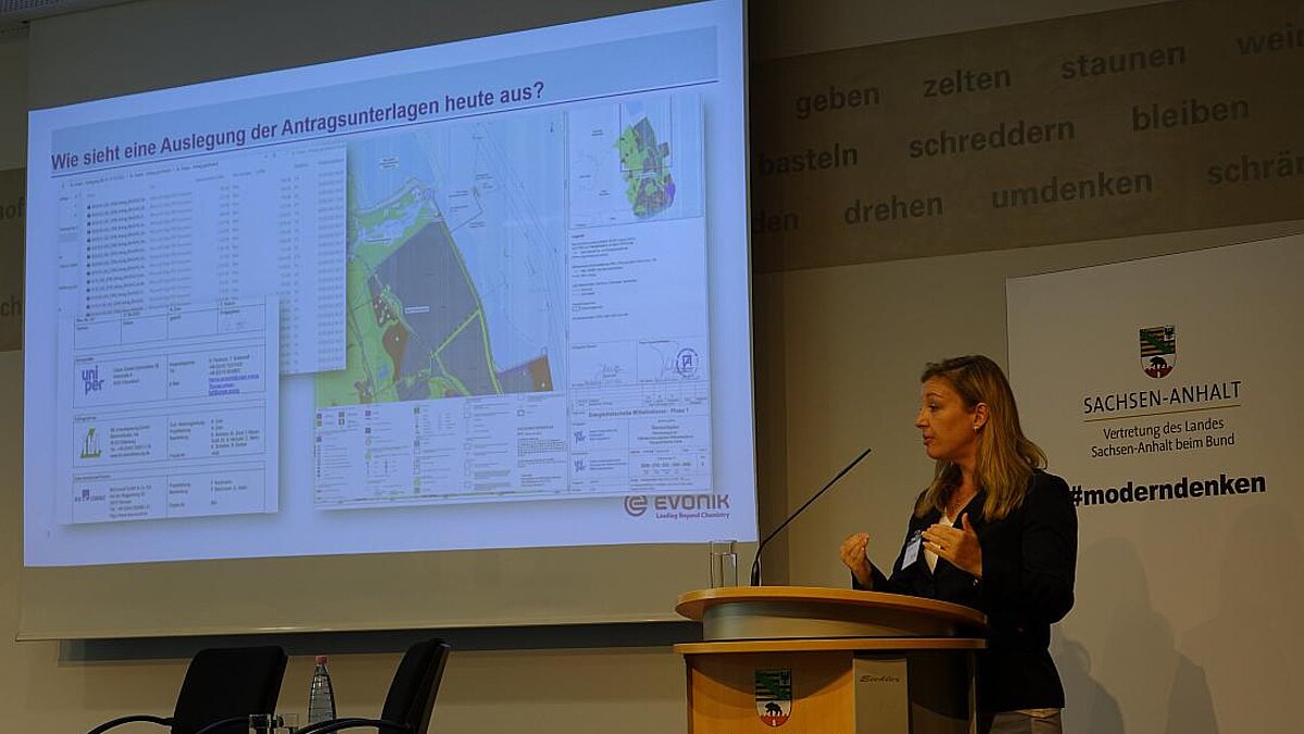 Screen and woman with blonde hair at the lectern