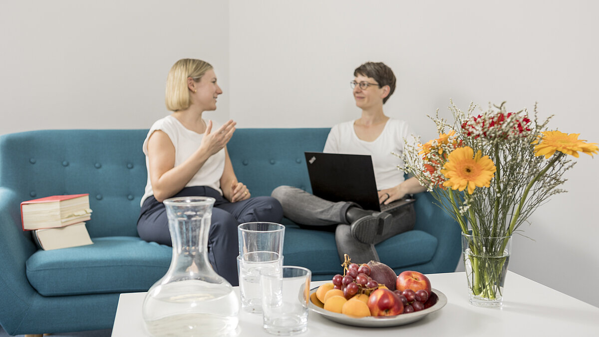 Zwei Mitarbeiterinnen des FÖV auf einem türkisblauen Sofa im Gespräch.