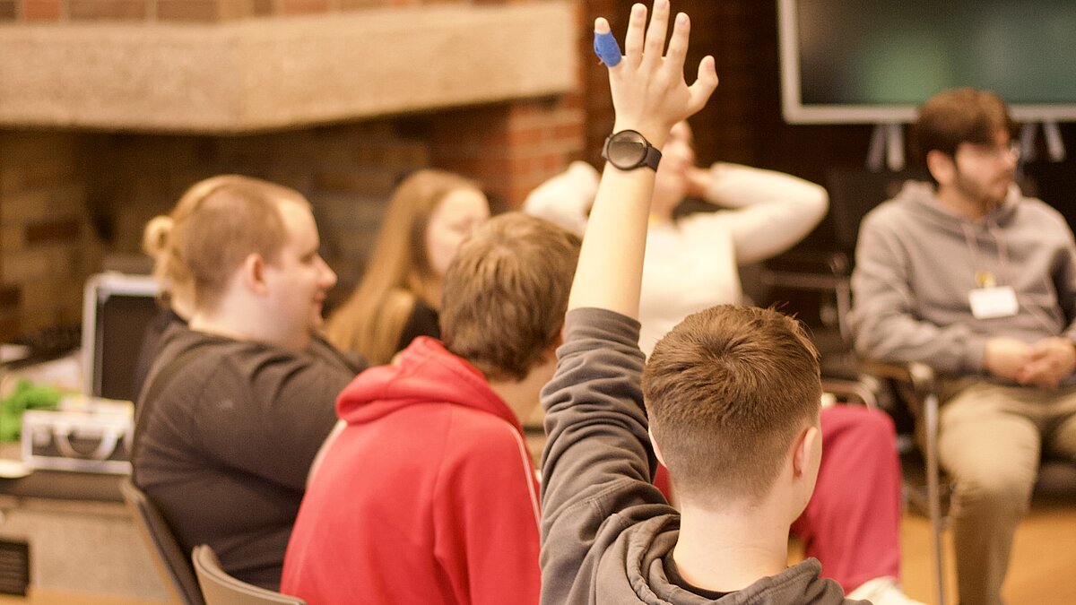 Group of young people in a workshop. One person raises their hand.