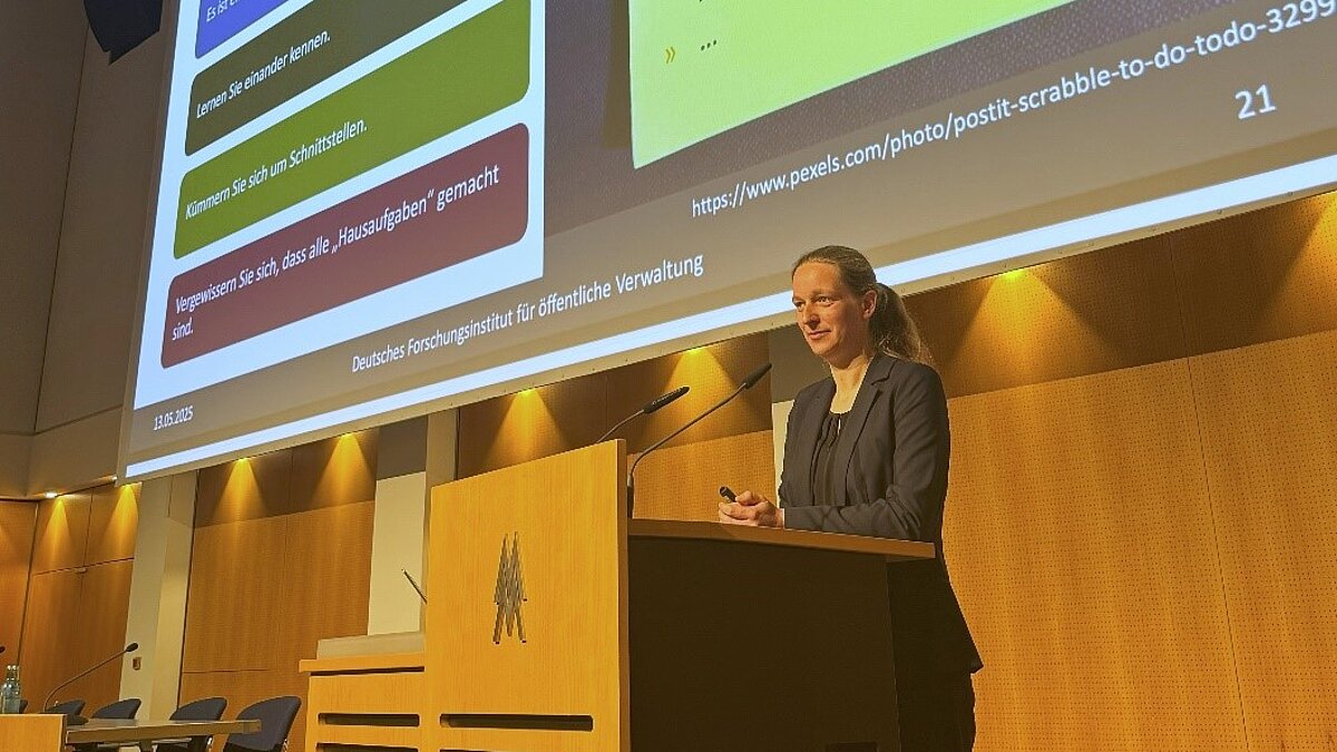 Jenny Rademann am Rednerpult. Im Hintergrund ist auf einer Leinwand das Beamerbild zu sehen.