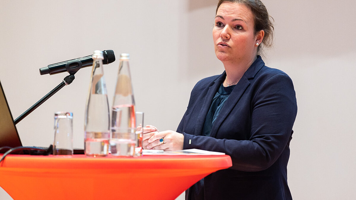 Woman with microphone in front of red bar table.