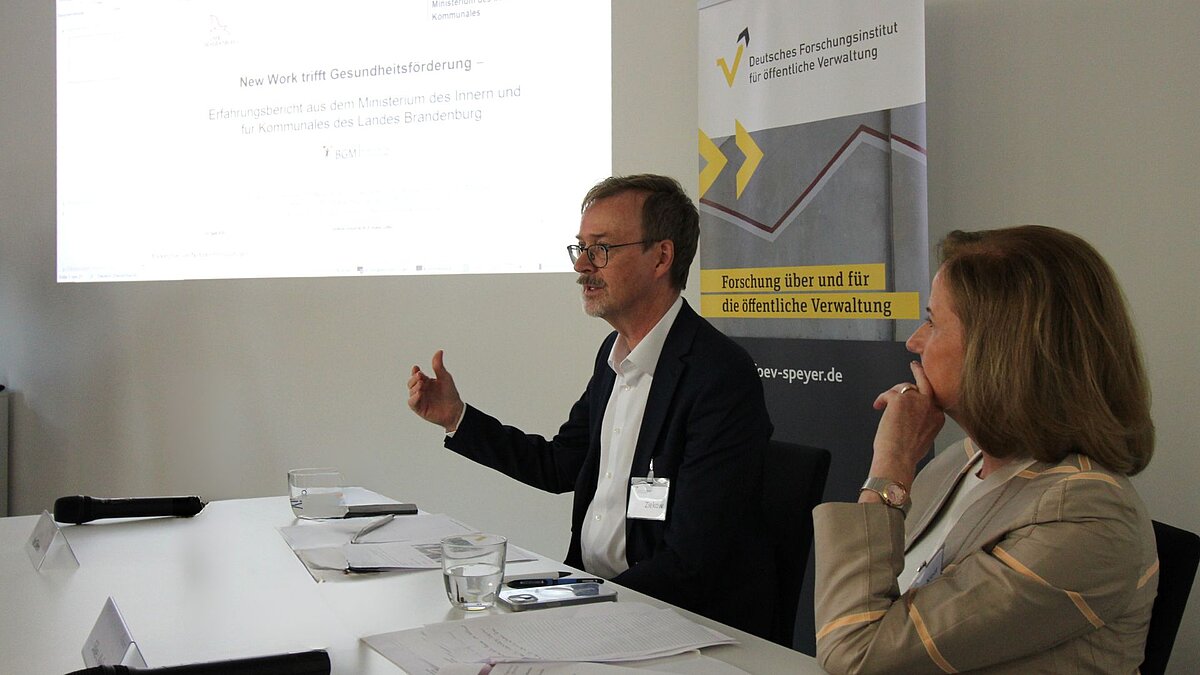 Der Direktor des Instituts, Prof.  Jan Ziekow, und die Geschäftsführerin, Dr. Silke I. Keil sitzen am Tisch vor einem Beamerbild