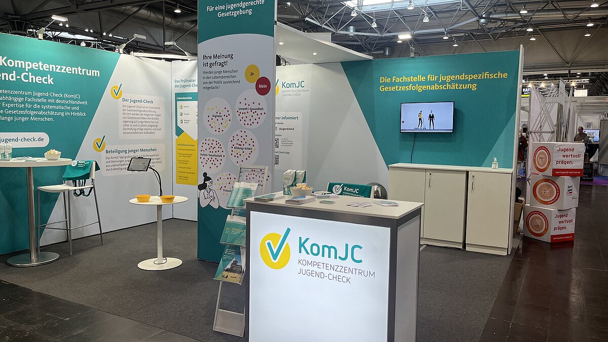Image of the ComYC fair stand in the colors petrol and yellow. A counter with the ComYC-logo is positioned at the front.