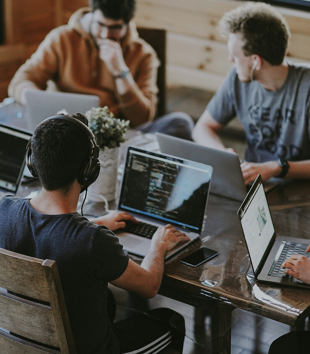 Eine Gruppe von Personen sitzt an einem Tisch und arbeitet an Laptops