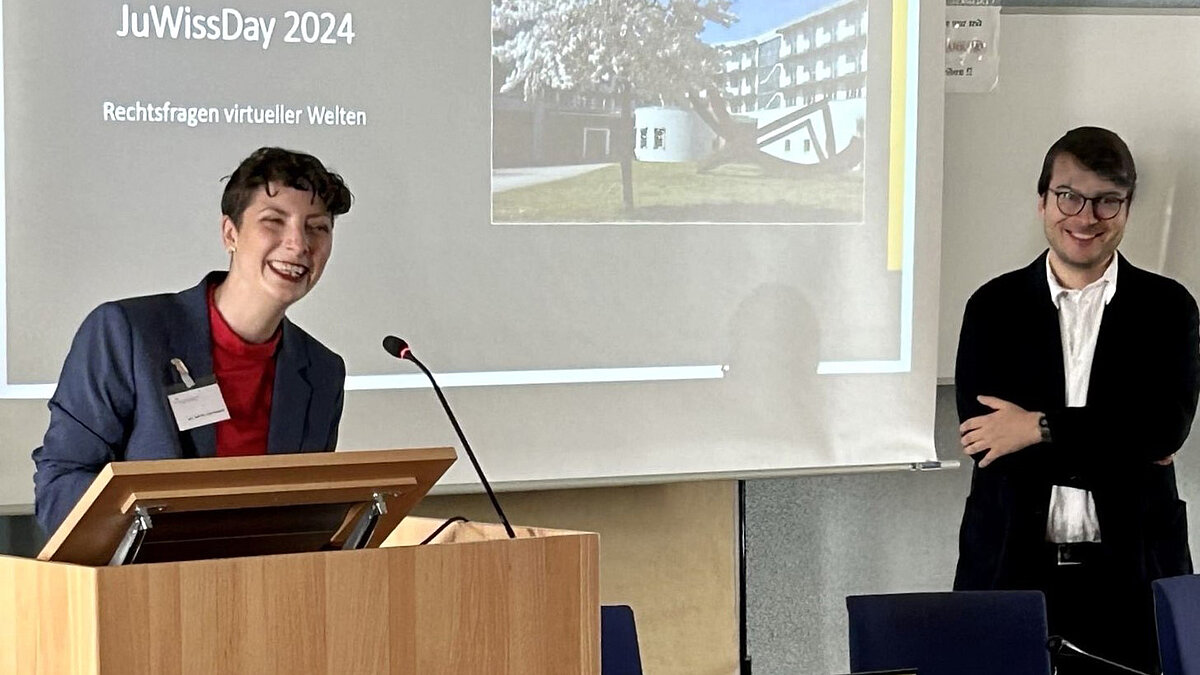 Dr. Sarah Hartmann (University of Münster) and Dr. Jonas Botta (NIPAG Speyer) at the lectern in front of a presentation on JuWissDay 2024
