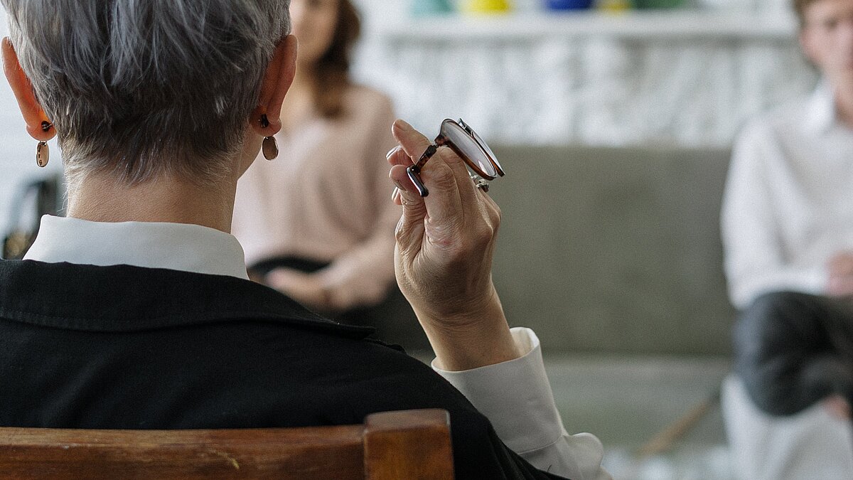 [Translate to English:] sitzende Person von hinten mit einer Brille in der Hand