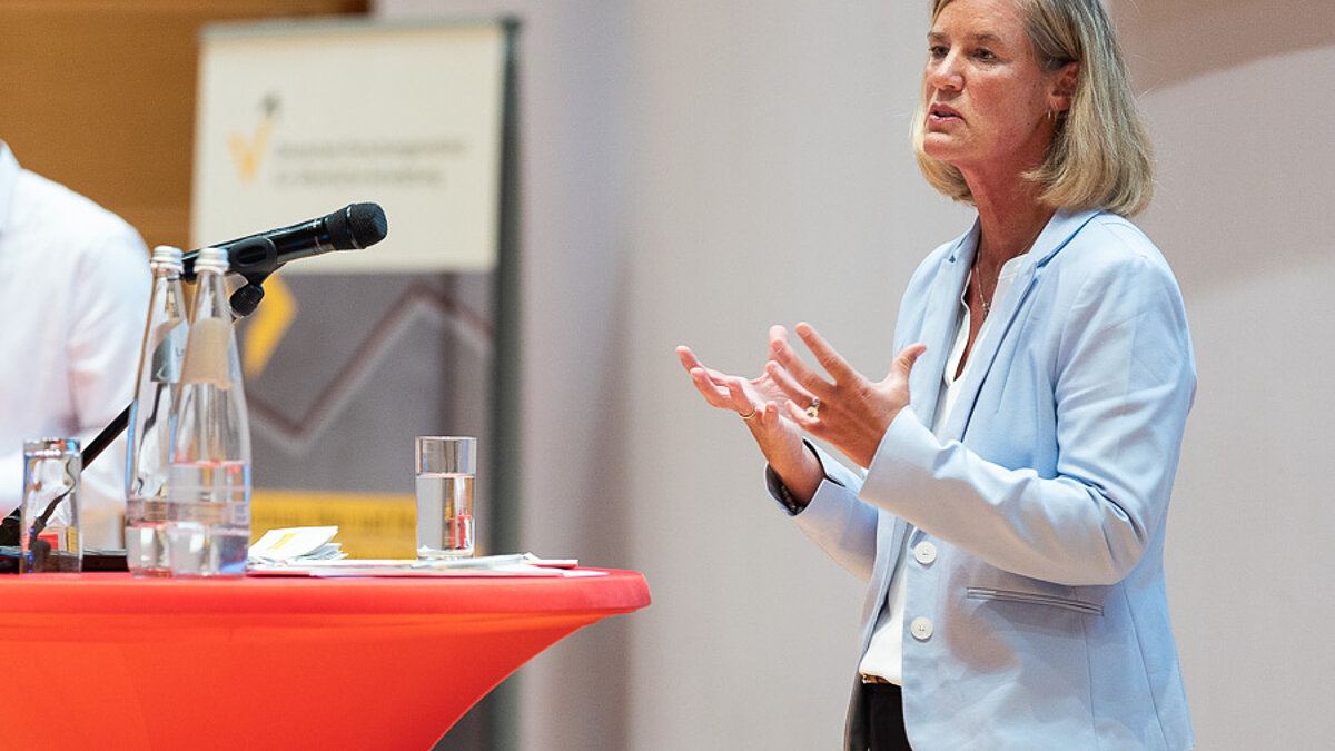 Woman with a light blue jacket in front of a red bar table.