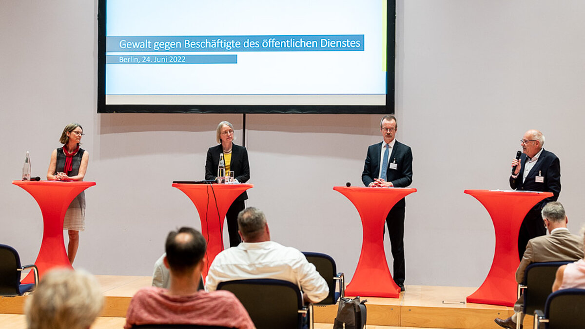 Panel guests at red bar tables in front of the screen.
